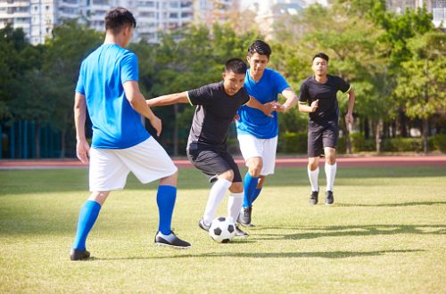 a group of young asian soccer football player playing on outdoor court.